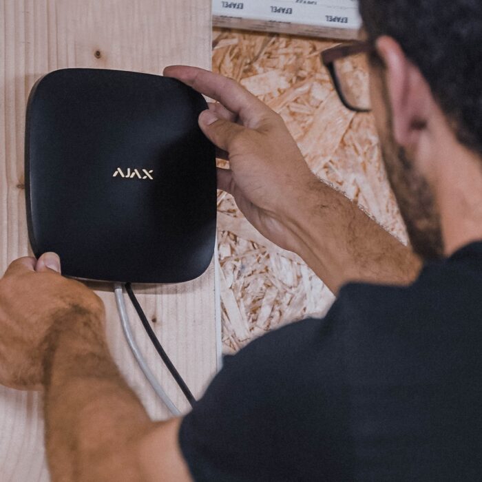 Técnico a instalar uma central de alarme Ajax numa parede durante a montagem de um sistema de segurança.